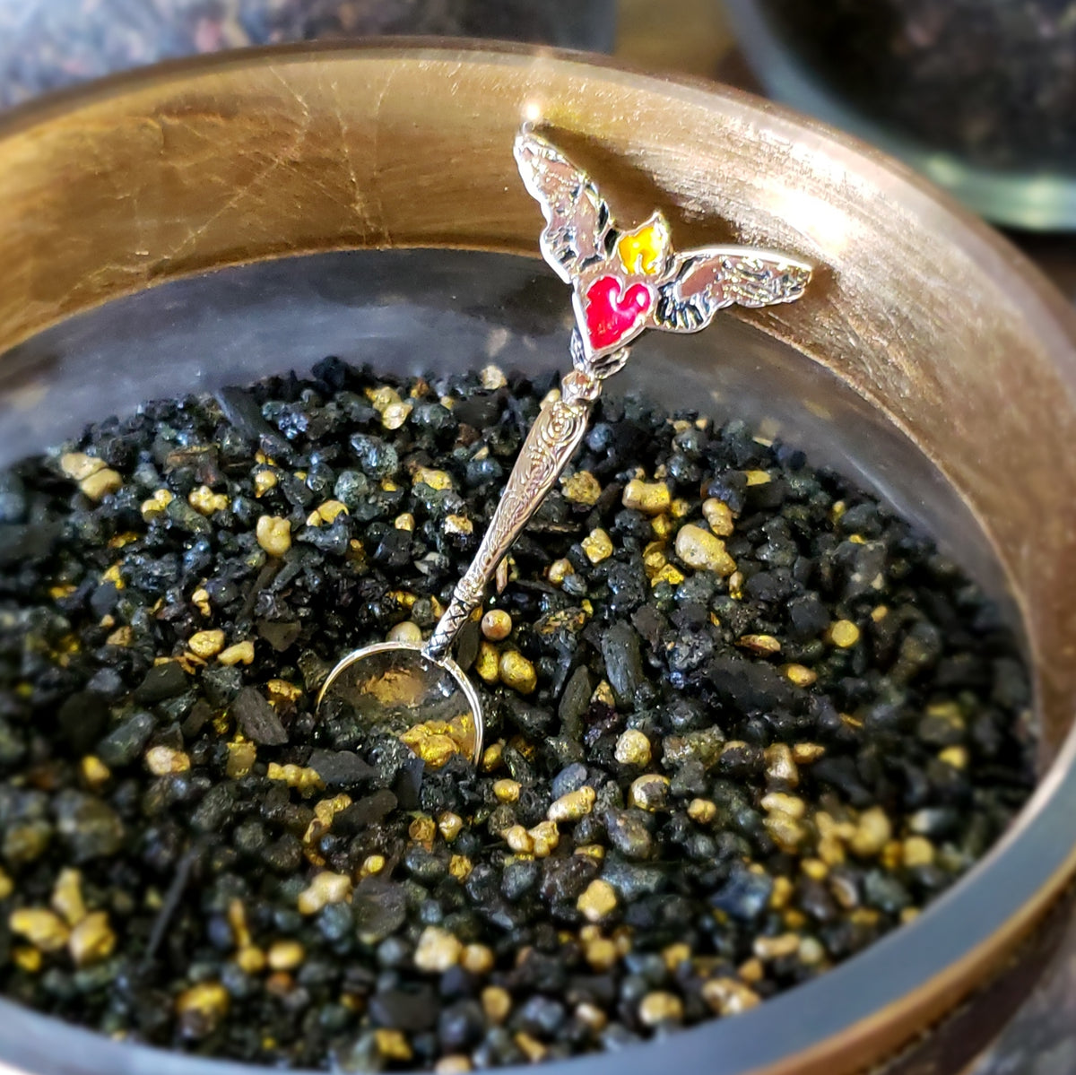 Milagros Nero Oro resin incense in a brass burner bowl with a heart-charm dosing spoon.