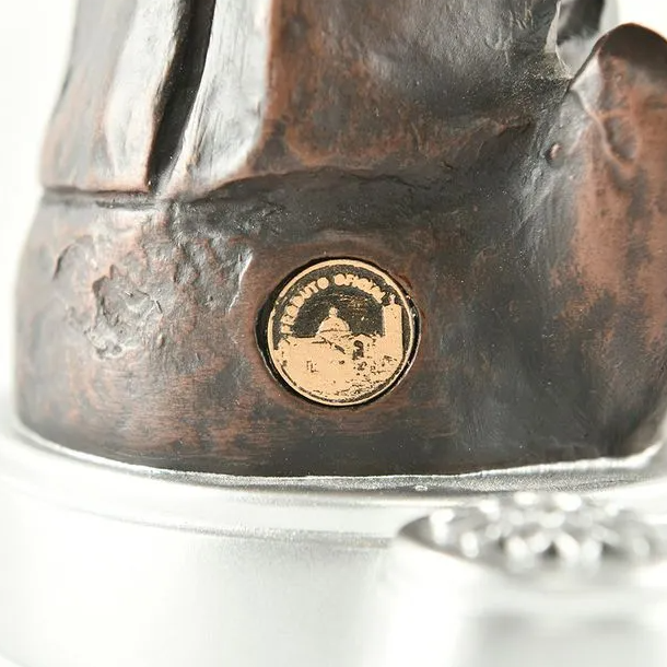 Close-up of a bronze sculpture with a gold emblem on a white background